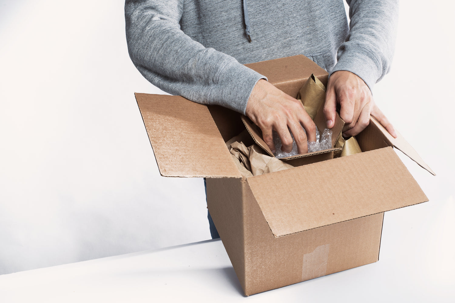 Bild: Man sieht einen Mann, welcher gerade ein braunes Paket öffnet, dies soll auf Versand hinweisen.